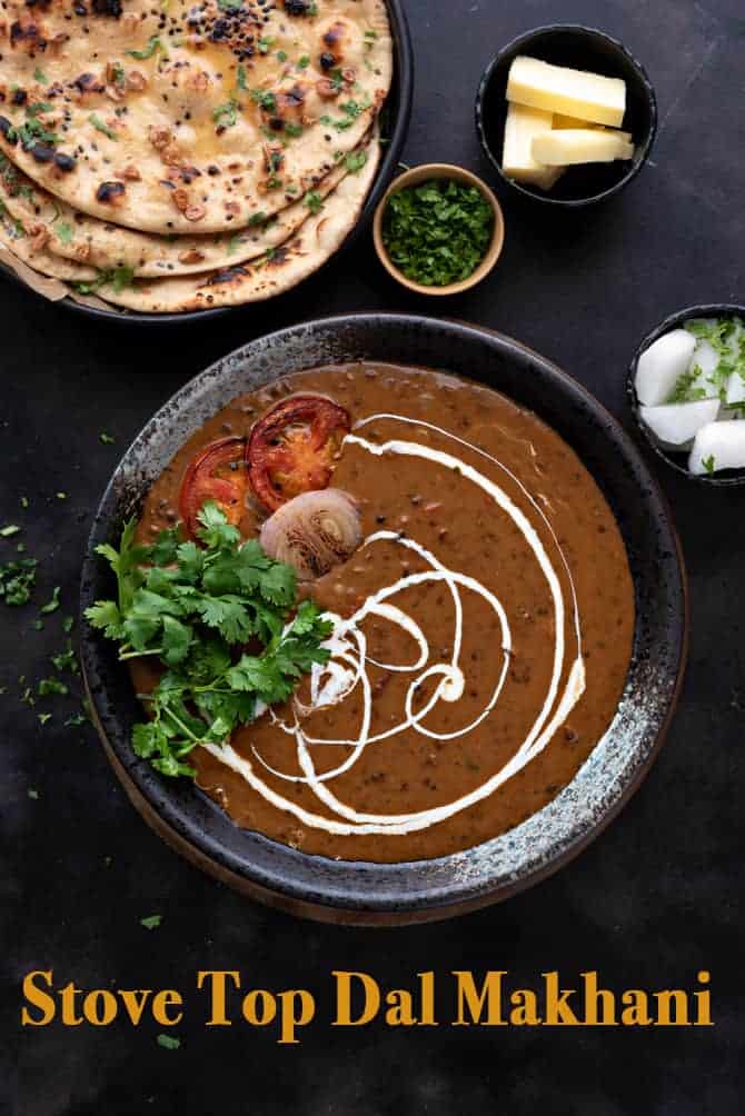 Overhead shot of dal makhani served in black bowl with naan bread and butter on side.