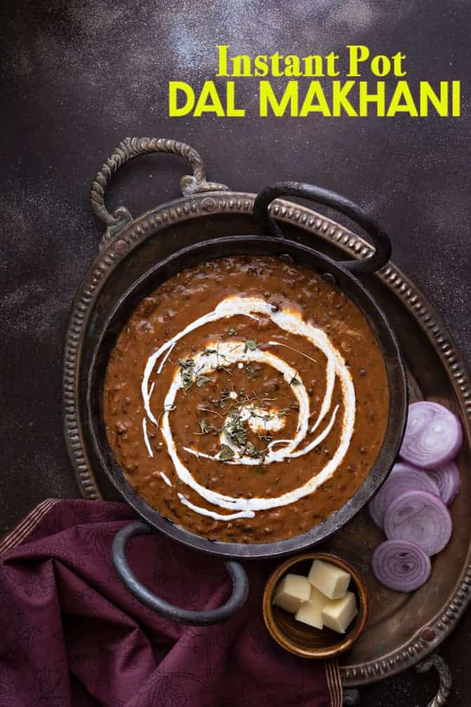 Overhead shot of dal makhani served in traditional kadhai with onion rings and butter on the side.