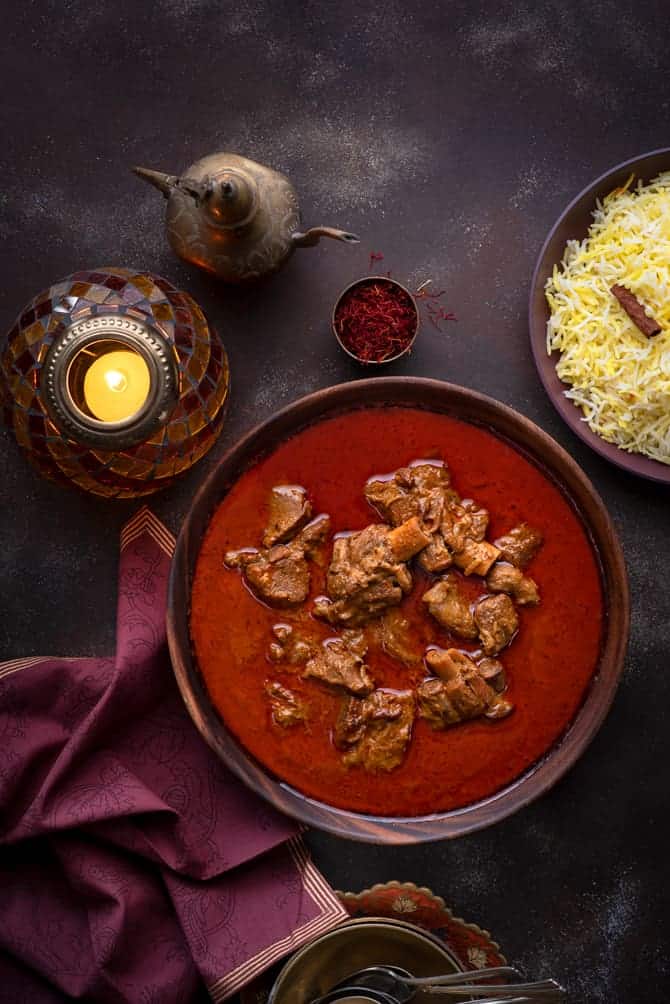 Overhead shot of Mutton Korma or Lamb Korma in wooden bowl with saffron rice on the side.