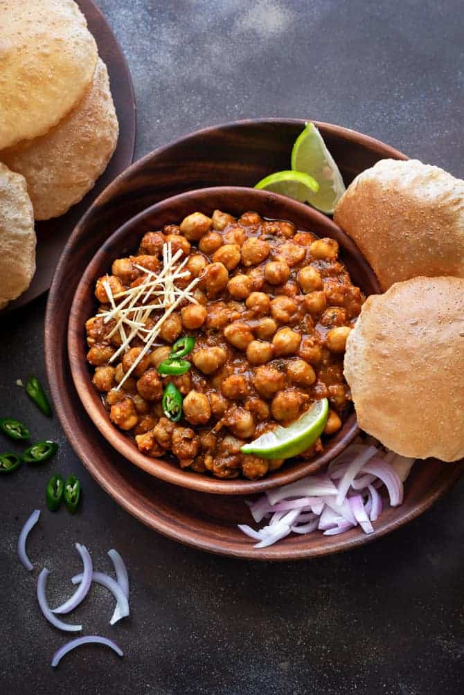 Chana Masala or chole served in wooden bowl along with puris, lemon wedges and onions on the side.