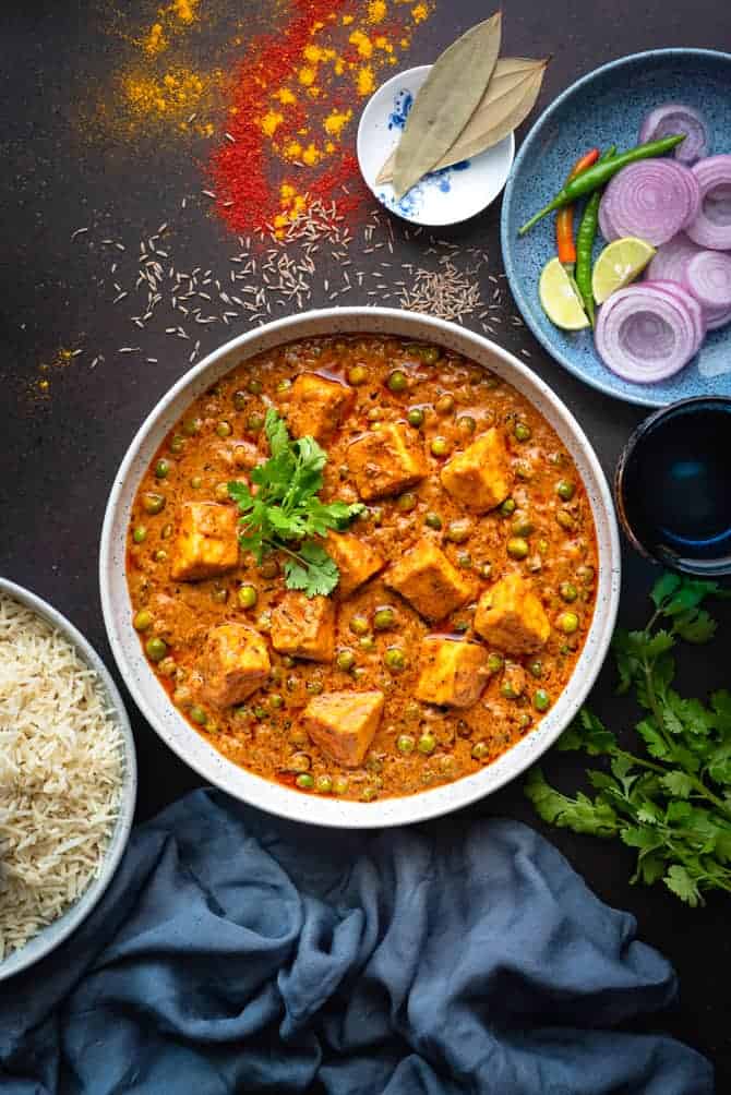Overhead shot of Matar paneer in large white bowl with rice and onions ring on the side