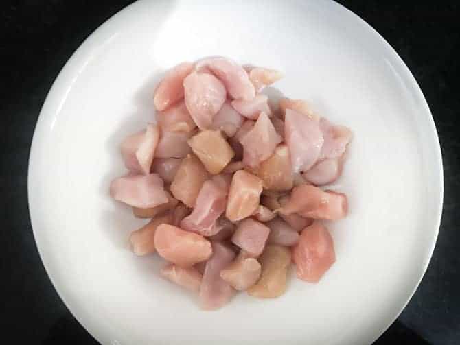 Bite sized boneless chicken cubes in white bowl to make chicken pakora recipe