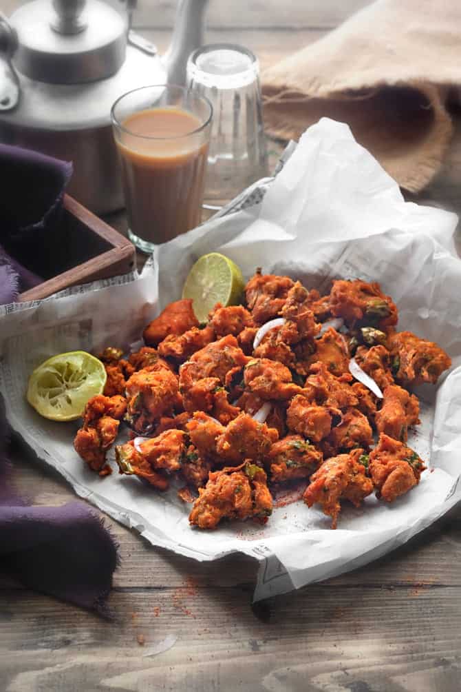 Crispy chicken pakora or chicken fritters on parchment lined paper, tea glass at the back.