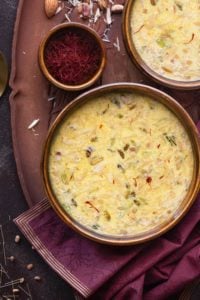 Sheer Korma in two brown bowls, saffron in a small bowl on wooden tray.