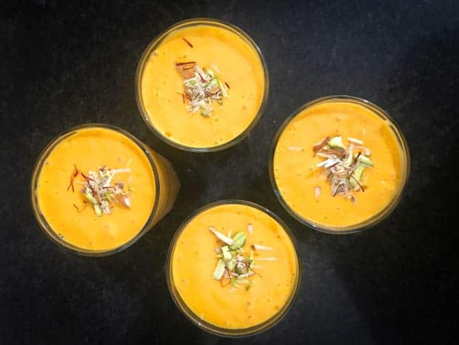 Mango lassi served in 4 glasses and garnished with saffron strands and slivered nuts.