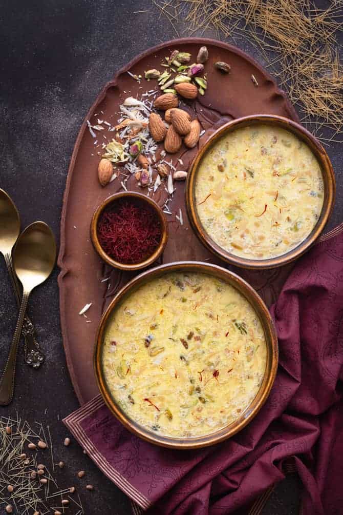 Sheer Korma in two brown bowls, saffron in a small bowl on wooden tray.