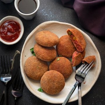 Crisp mixed veg cutlet on white plate with one cutlet cut open, sauce and soft drink on the side.