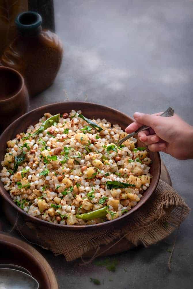 Sabudana khichdi in wooden bowl, kid's hand holding spoon kept into it.