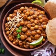 Close up shot of Chana Masala or chole in wooden bowl with puris, onions and lemon wedges.