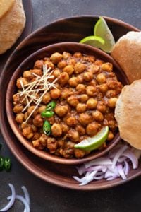 Close up shot of Chana Masala or chole in wooden bowl with puris, onions and lemon wedges.