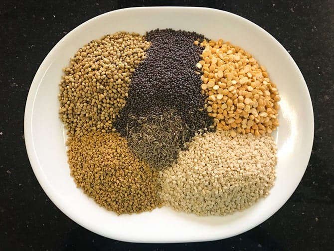 Lentils, mustard, cumin, fenugreek and coriander seeds on white plate for the making of sambar powder recipe.