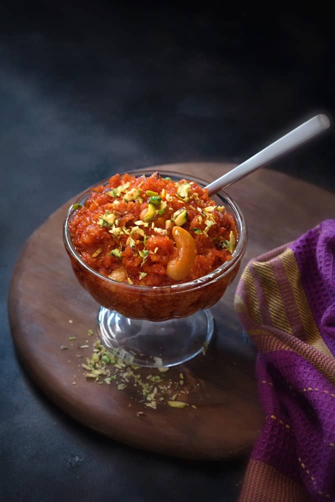 Traditional gajar ka halwa or carrot halwa in a glass bowl, with a spoon into it.
