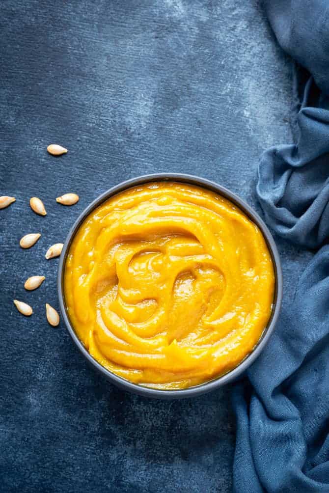Homemade pumpkin puree in blue bowl, some pumpkin seeds spread around.