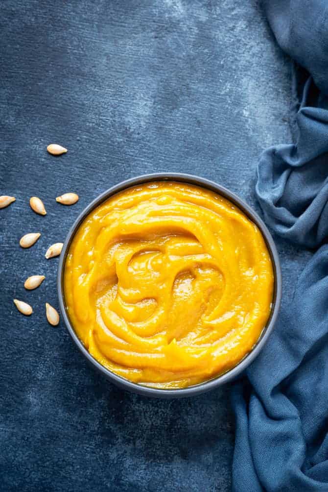 Homemade pumpkin puree in blue bowl, some pumpkin seeds spread around.