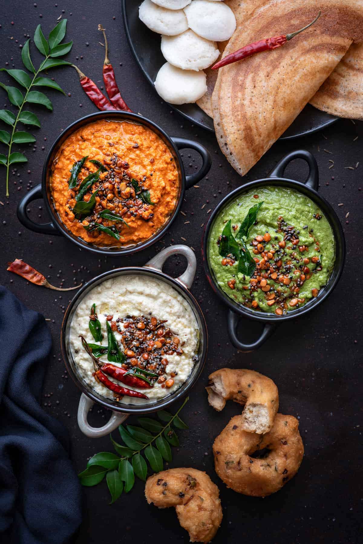 3 different types of South Indian coconut chutney served in 3 different black bowls.