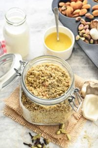 Close up shot of dry fruits powder in glass jar with nuts and milk on the side.