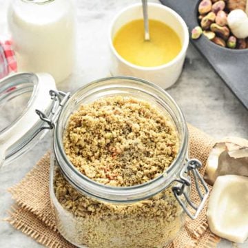 Close up shot of dry fruits powder in glass jar with nuts and milk on the side.