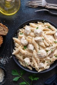 Close up shot of chicken Alfredo pasta served in a black plate.