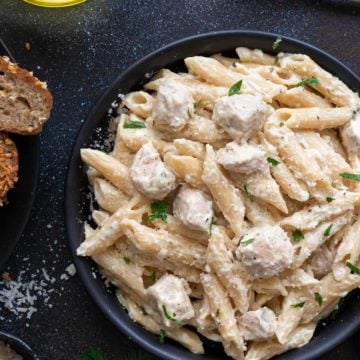 Close up shot of chicken Alfredo pasta served in a black plate.