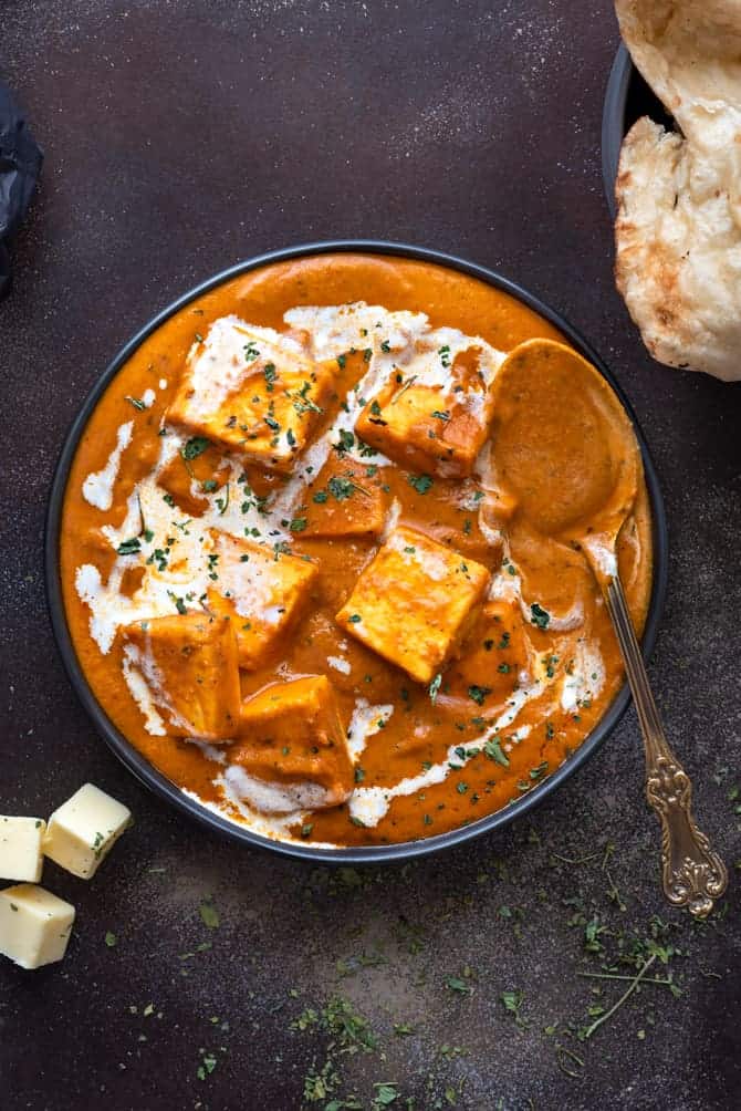 Close up shot of paneer butter masala served in a black plate with a spoon.