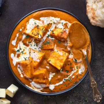 Restaurant style paneer butter masala gravy served in a black plate with a spoon.