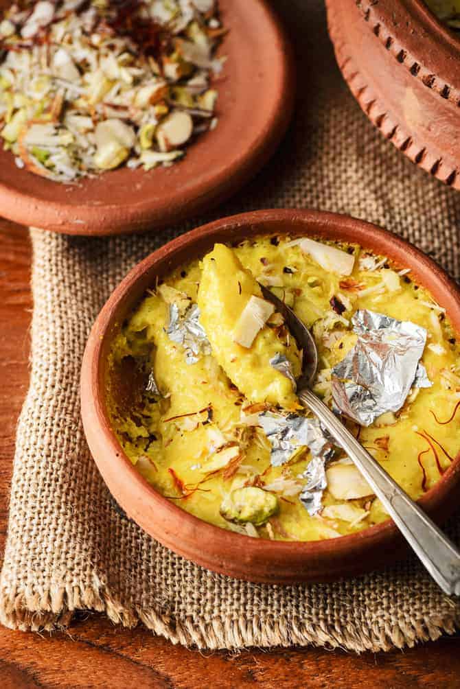 Close up shot of kesar phirni sweet in earthen pot with a spoon.