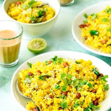 Close up shot of onion poha on a green plate and in bowl at the back, tea in glass on the side.