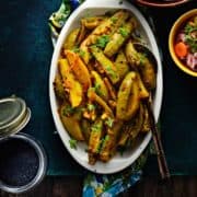 Aloo parwal in white oval plate with achari masala in a bowl, salad, roti and some spice on the side.