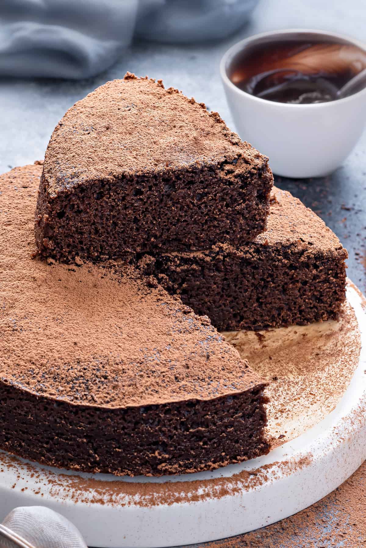 Close up shot of moist eggless chocolate cake on plate with white bowl in the background.