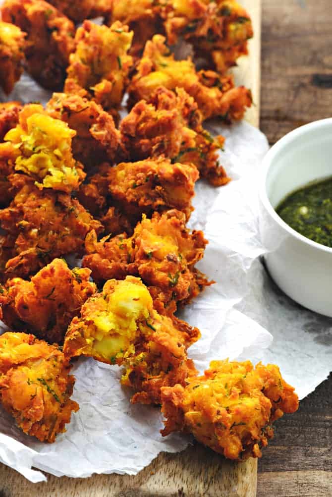 Close up shot of corn paneer pakoda on butter paper placed on wooden platter.