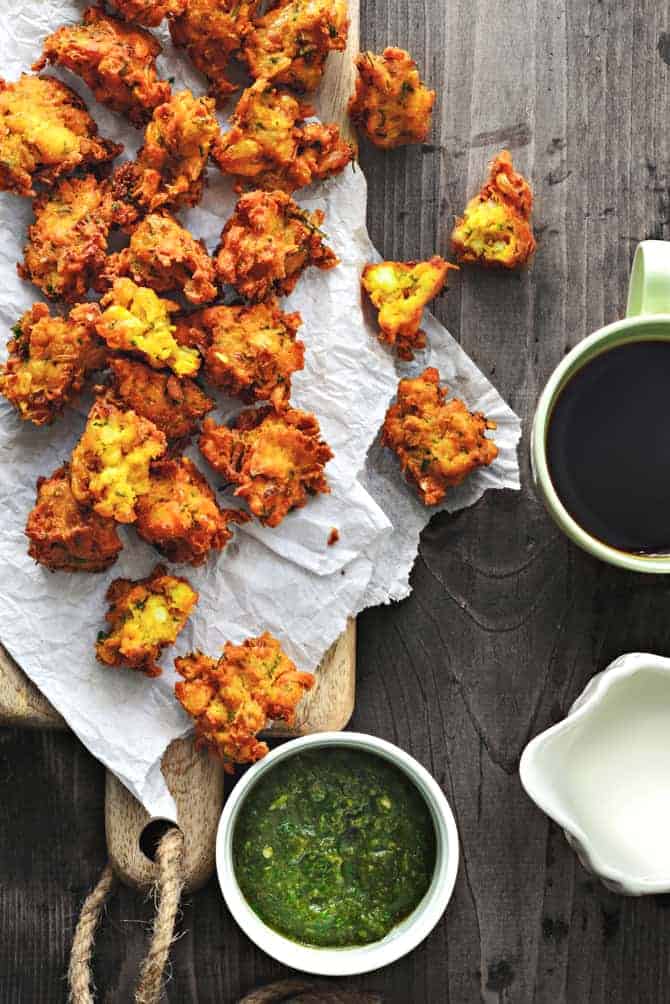 Corn paneer pakoda on butter paper over the wooden board, chutney and tea on the side.