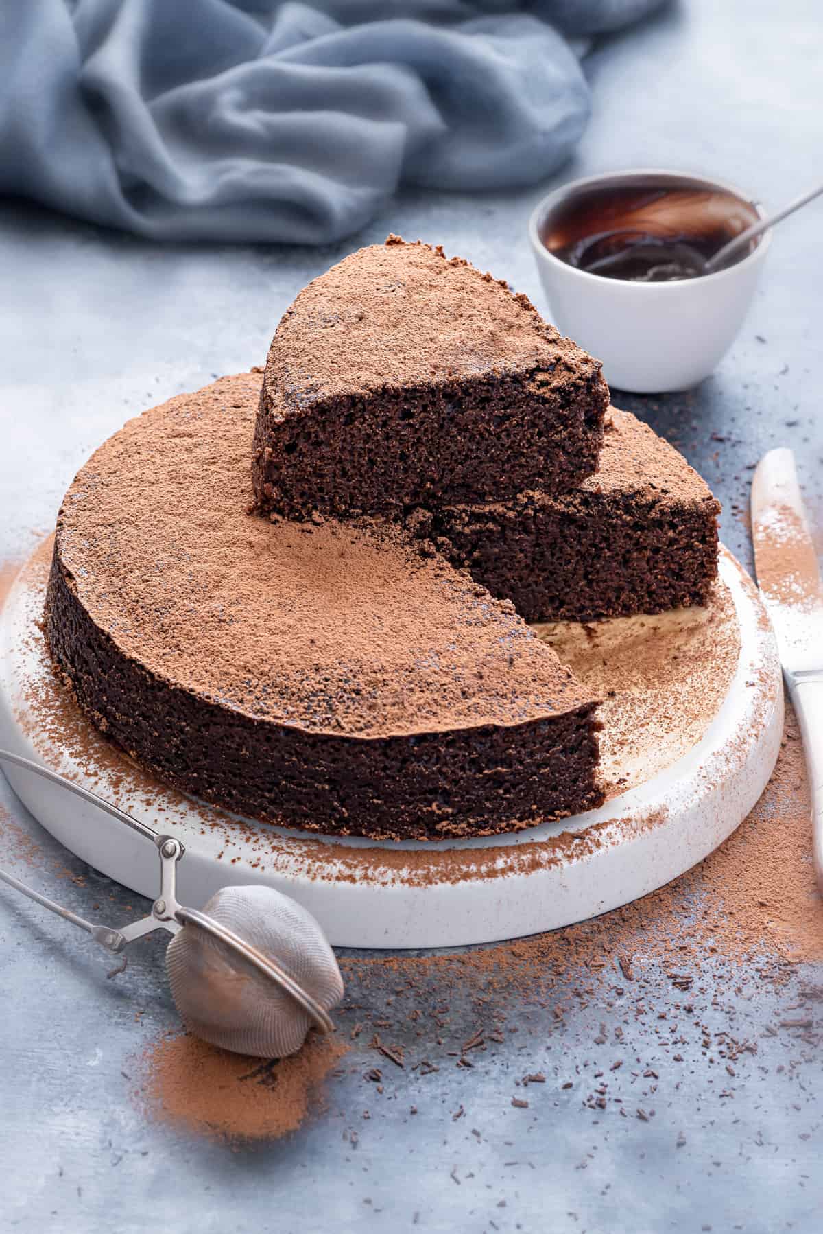 Eggless chocolate cake on white plate with one cut slice on the top of the cake.