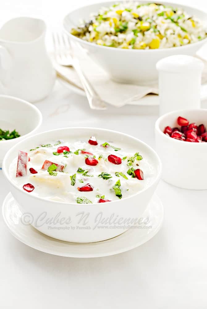 Mix Fruit Raita served in white bowl, rice pilaf and pomegranate in bowl at the back.