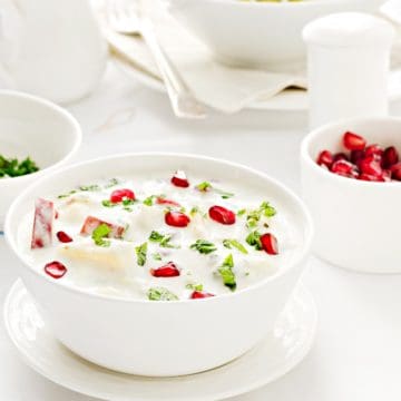 Mix Fruit Raita served in white bowl, rice pilaf and pomegranate in bowl at the back.