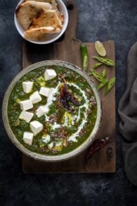 Restaurant style palak paneer curry in grey ceramic bowl, naan bread on the side.