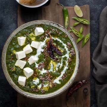 Restaurant style palak paneer curry in grey ceramic bowl, naan bread on the side.