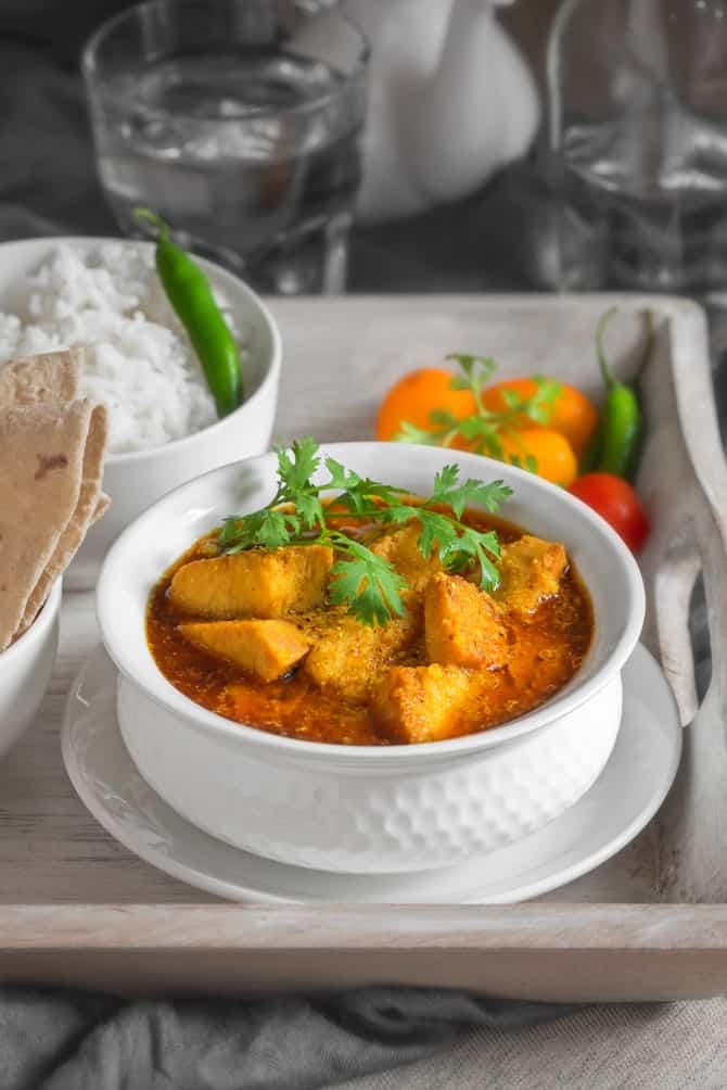 Close up shot of yam curry or Suran ki sabji in white bowl placed on wooden tray, roti and rice on the side.