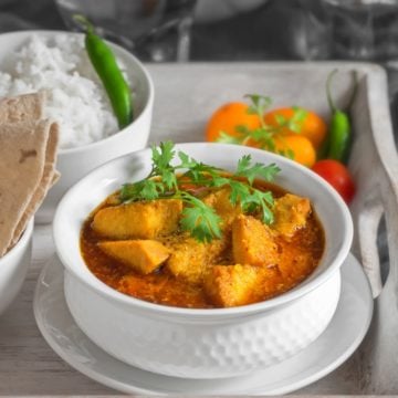 Close up shot of yam curry or Suran ki sabji in white bowl placed on wooden tray, roti and rice on the side.