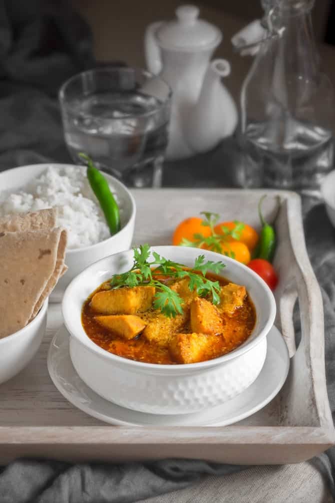 Yam curry or Suran sabzi in white bowl placed on wooden tray, roti and rice on the side.