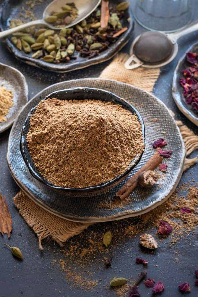 Close up shot of Indian chai masala or tea masala in black bowl with spices and rose petals spread around.