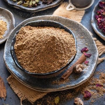 Close up shot of Indian chai masala or tea masala in black bowl with spices and rose petals spread around.