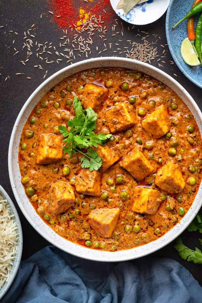 Close up shot of restaurant style matar paneer curry served in large white bowl.