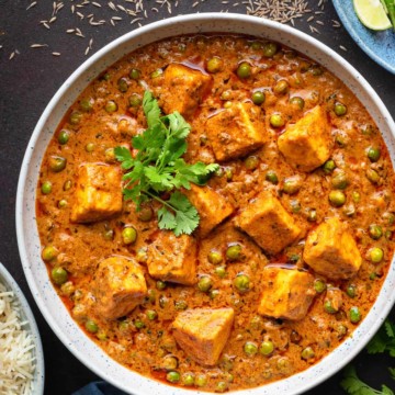 Close up shot of restaurant style matar paneer curry served in large white bowl.