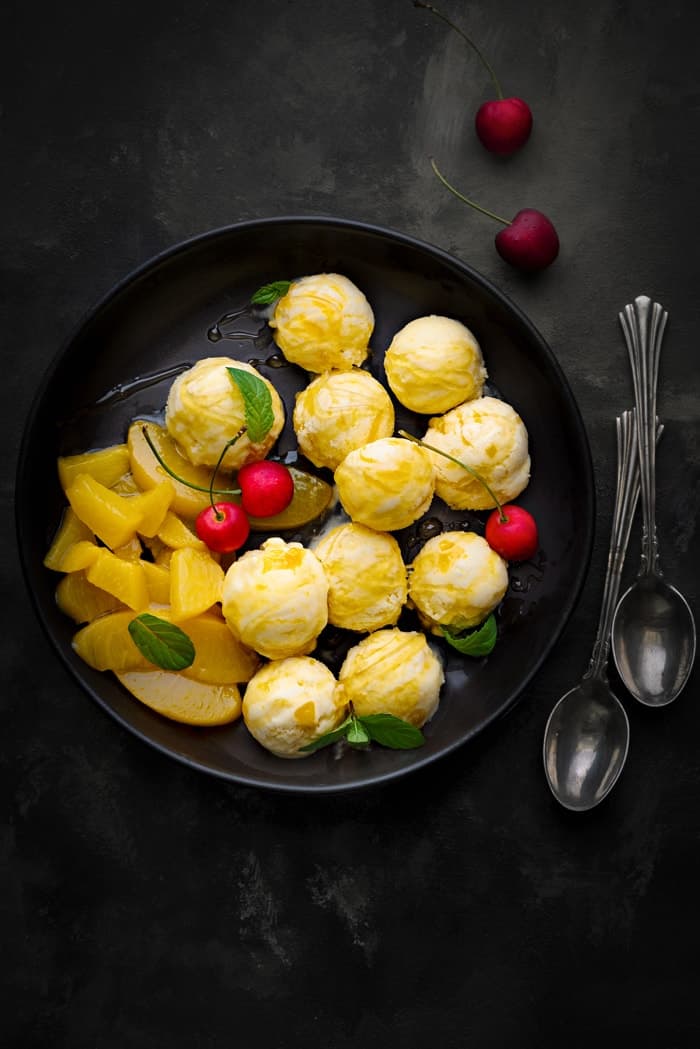 Overhead shot of peach frozen yogurt scoops on black plate with two spoon on the side.ead