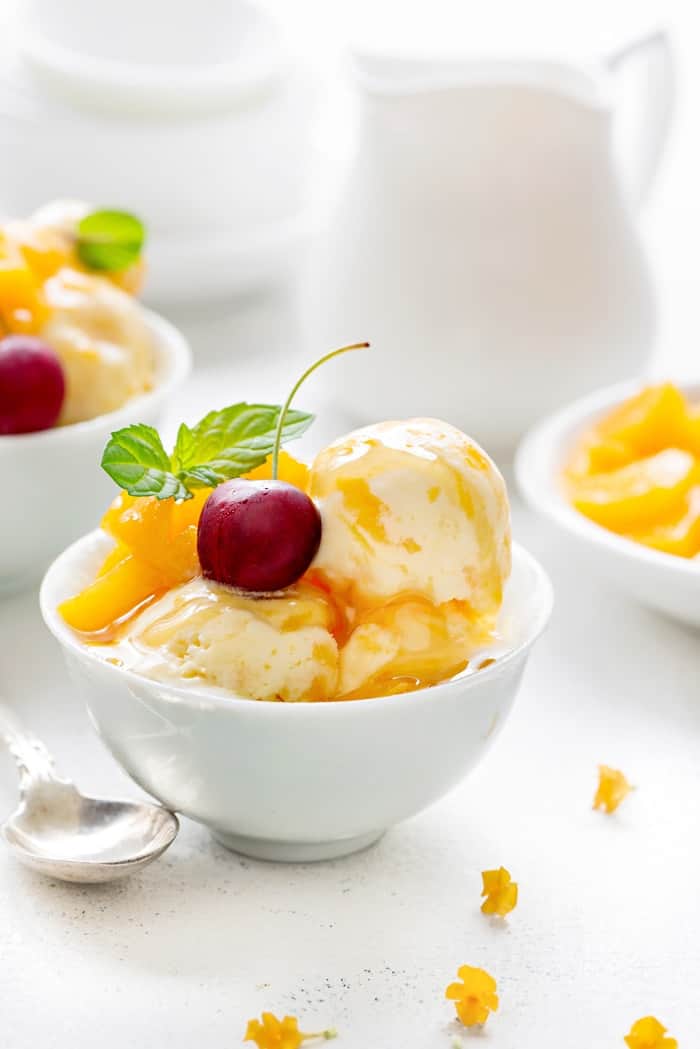 Close up shot pf peach frozen yogurt in white bowl with some tiny flowers spread around.