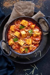 Close up shot of Kadai Paneer gravy served in small black iron karahi.