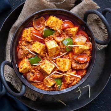 Close up shot of Kadai Paneer gravy served in small black iron karahi.