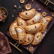 Overhead shot of flaky mawa gujiya sweet served in purple metal tray.