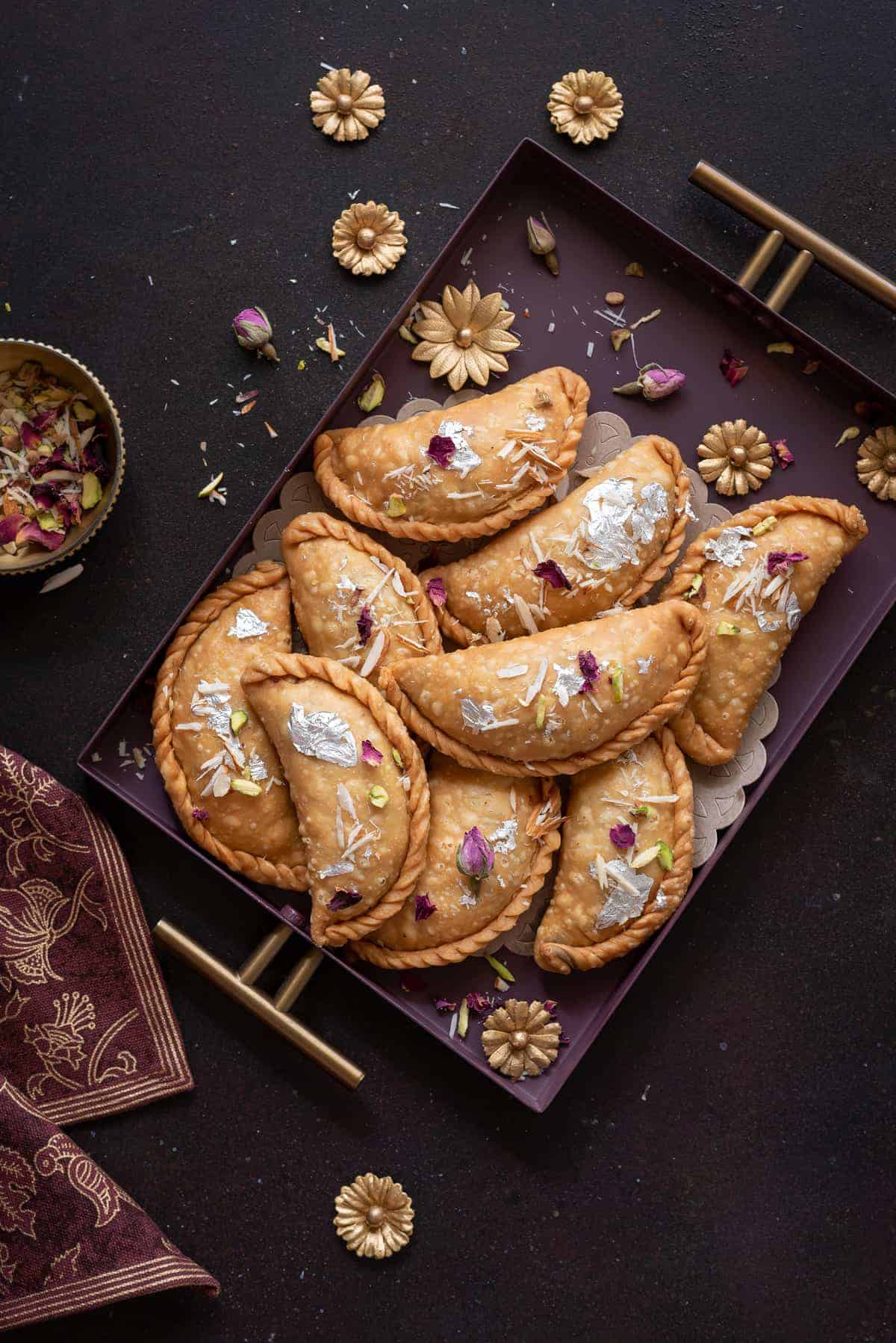 Overhead shot of flaky mawa gujiya sweet served in purple metal tray.