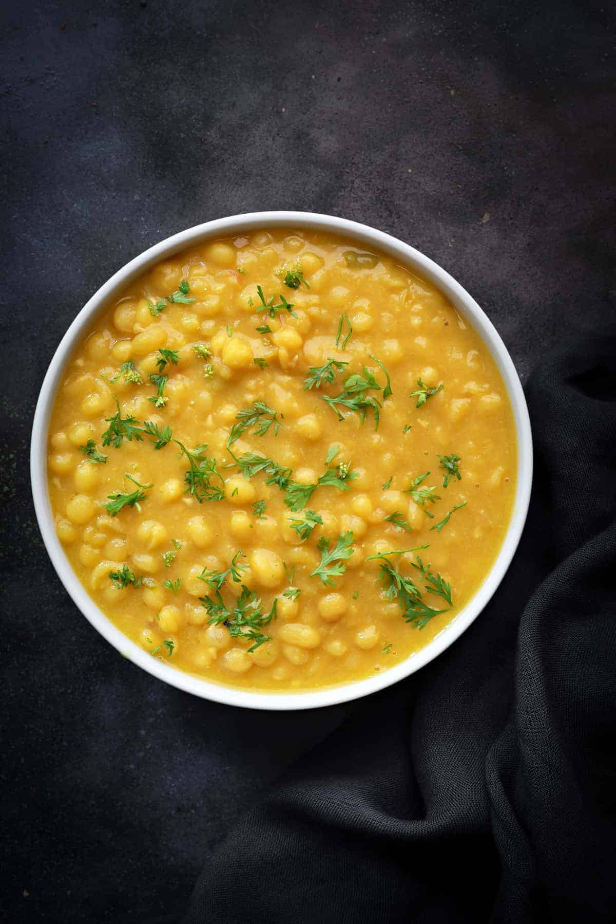 Delicious Ragda or white peas curry served in white bowl, black cotton linen at the side.